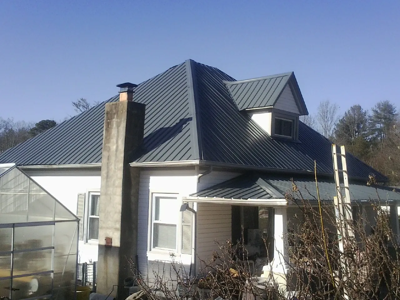 Dark blue standing seam metal roof on a white farmhouse with dormer — Slate & Tile Roof Repair by Roofing Brothers in Suffield