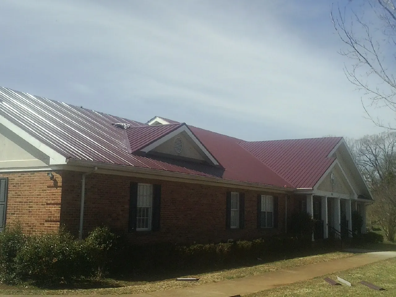 Red metal roof with gabled entries on a long brick building, from a Hail Damage Roof Repair job in Suffield